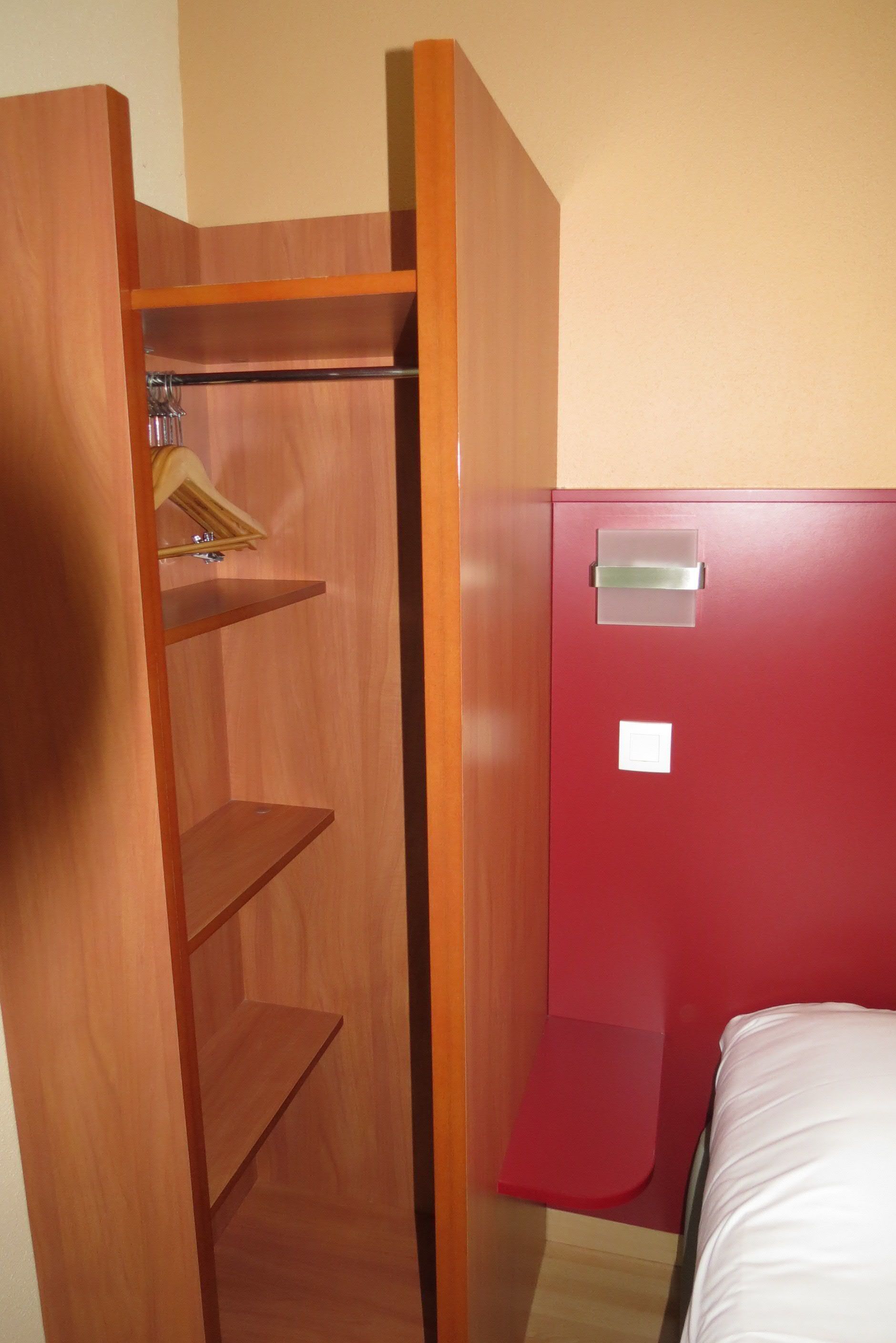 A room with a wooden wardrobe, a red cabinet, and a bed.