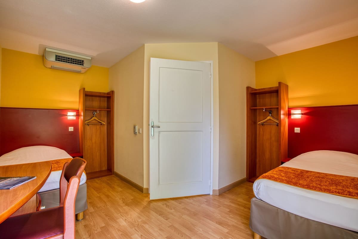 A hotel room with two beds, a desk, a chair, a wardrobe, and a door.