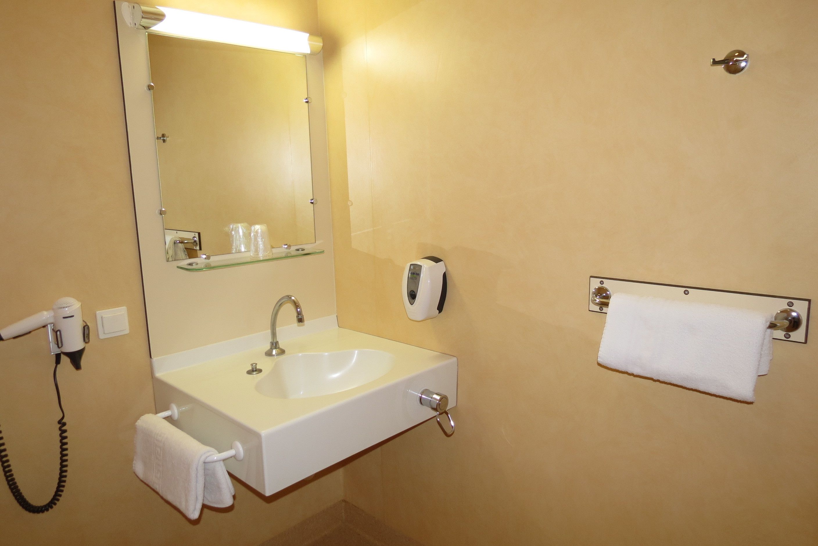 Een badkamer met een wit wastafel, een spiegel, een handdoekhouder en een haardroger.