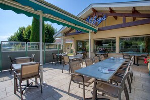 An outdoor patio area with multiple tables and chairs, a covered seating area, and a view of the surrounding landscape. - Abbys Hôtel (Carsac-Aillac)