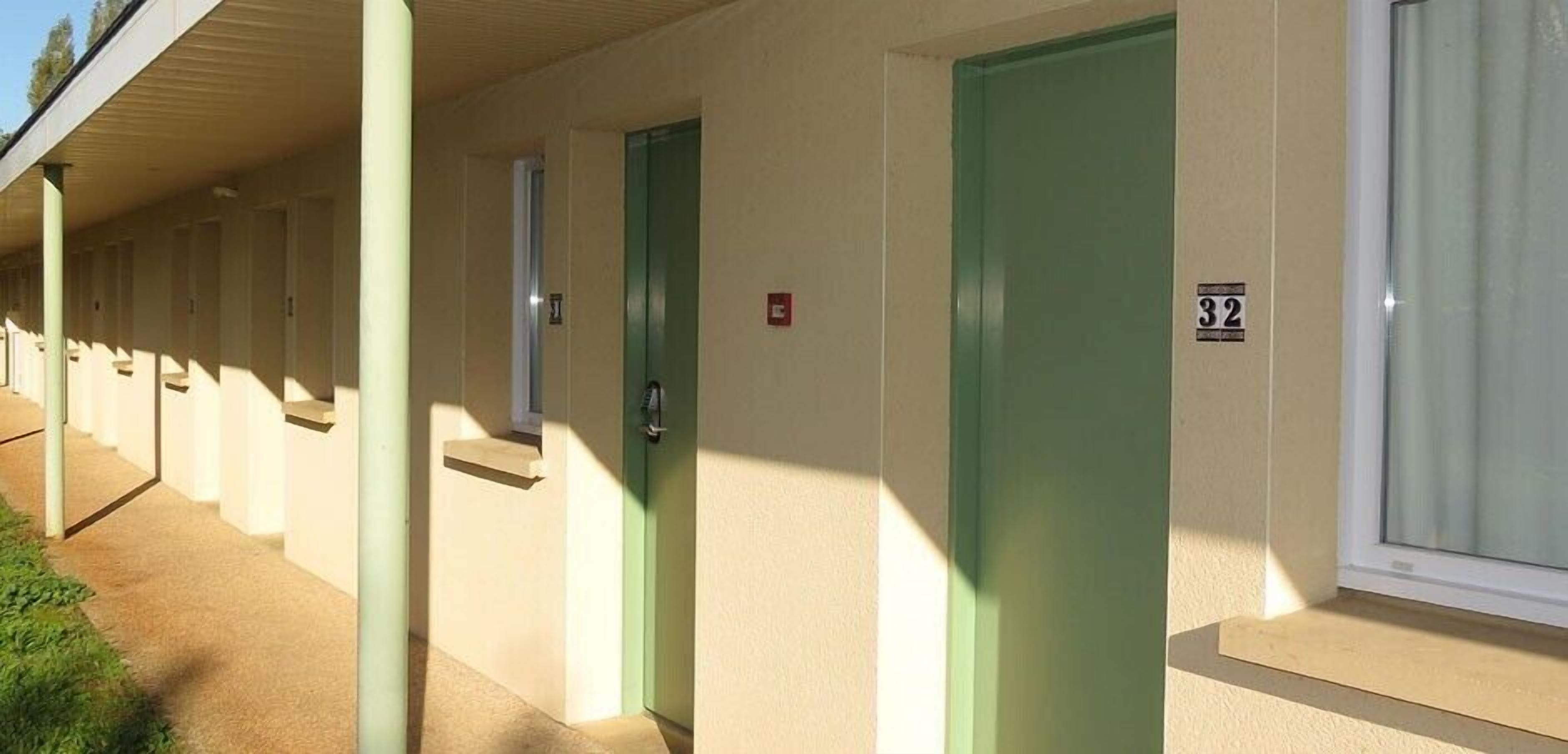 Una hilera de habitaciones de motel con puertas verdes y una ventana a la derecha.