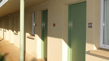Una hilera de habitaciones de motel con puertas verdes y una ventana a la derecha.