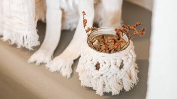 A white macrame stool with a glass vase containing dried flowers.