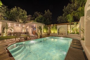 A swimming pool with a wooden deck, surrounded by greenery and stone walls.