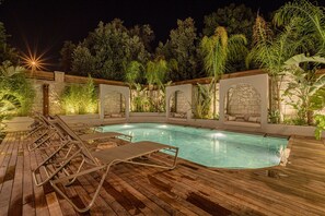 A poolside area with lounge chairs, a stone wall, and greenery.