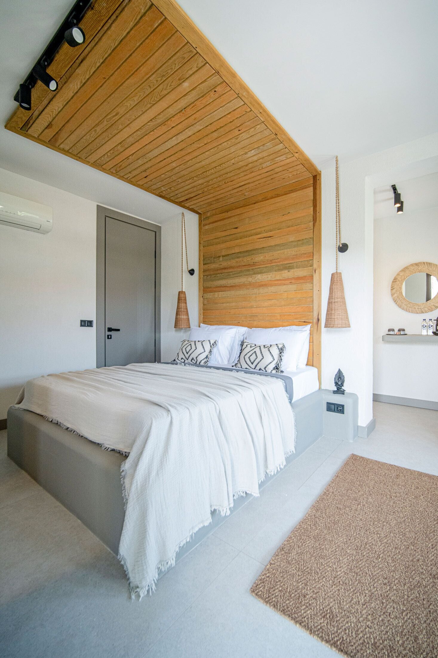 A modern bedroom with a wooden ceiling, a bed with patterned pillows, a bedside table, and a hanging lamp.