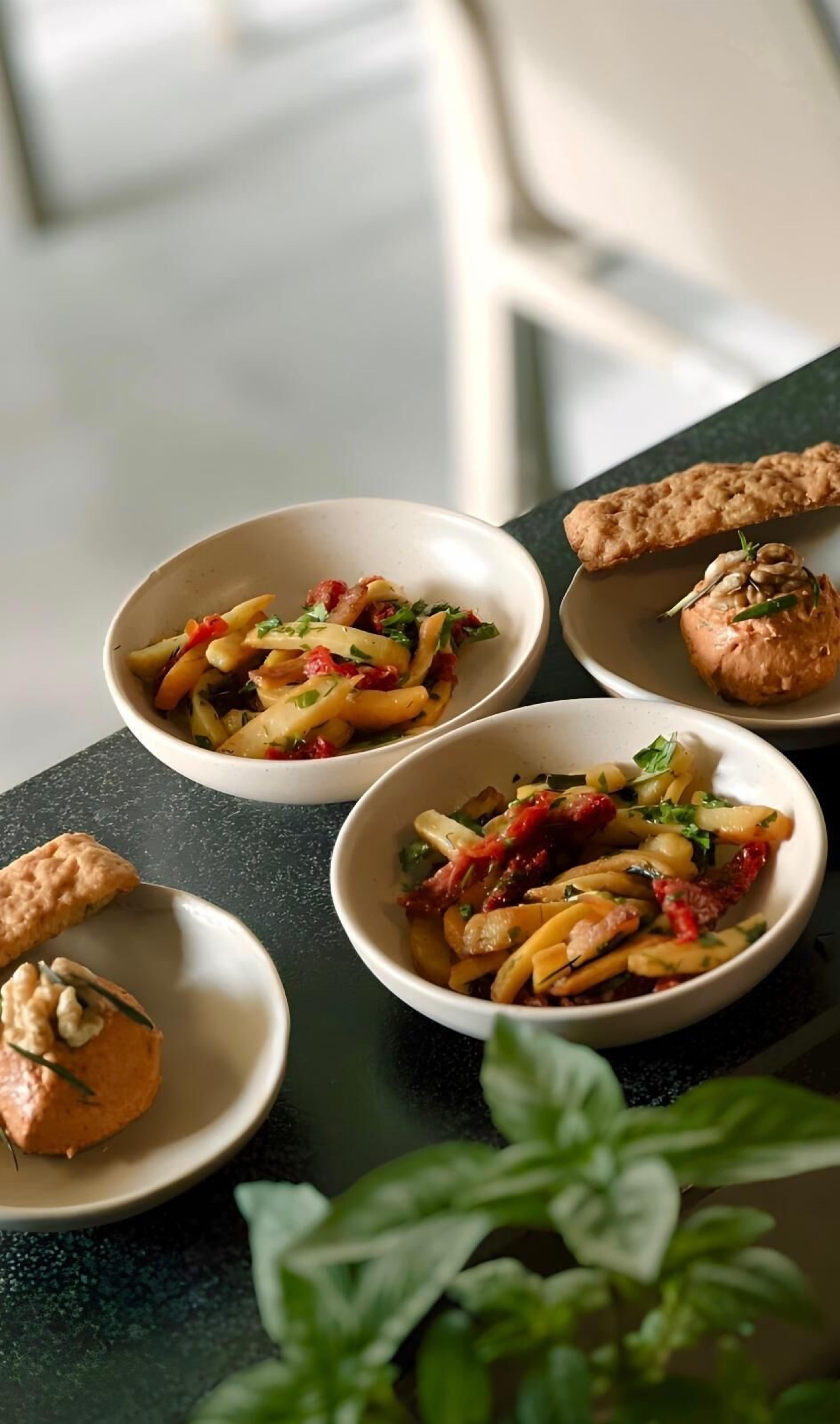 A table with three bowls of pasta salad and two small plates with bread.