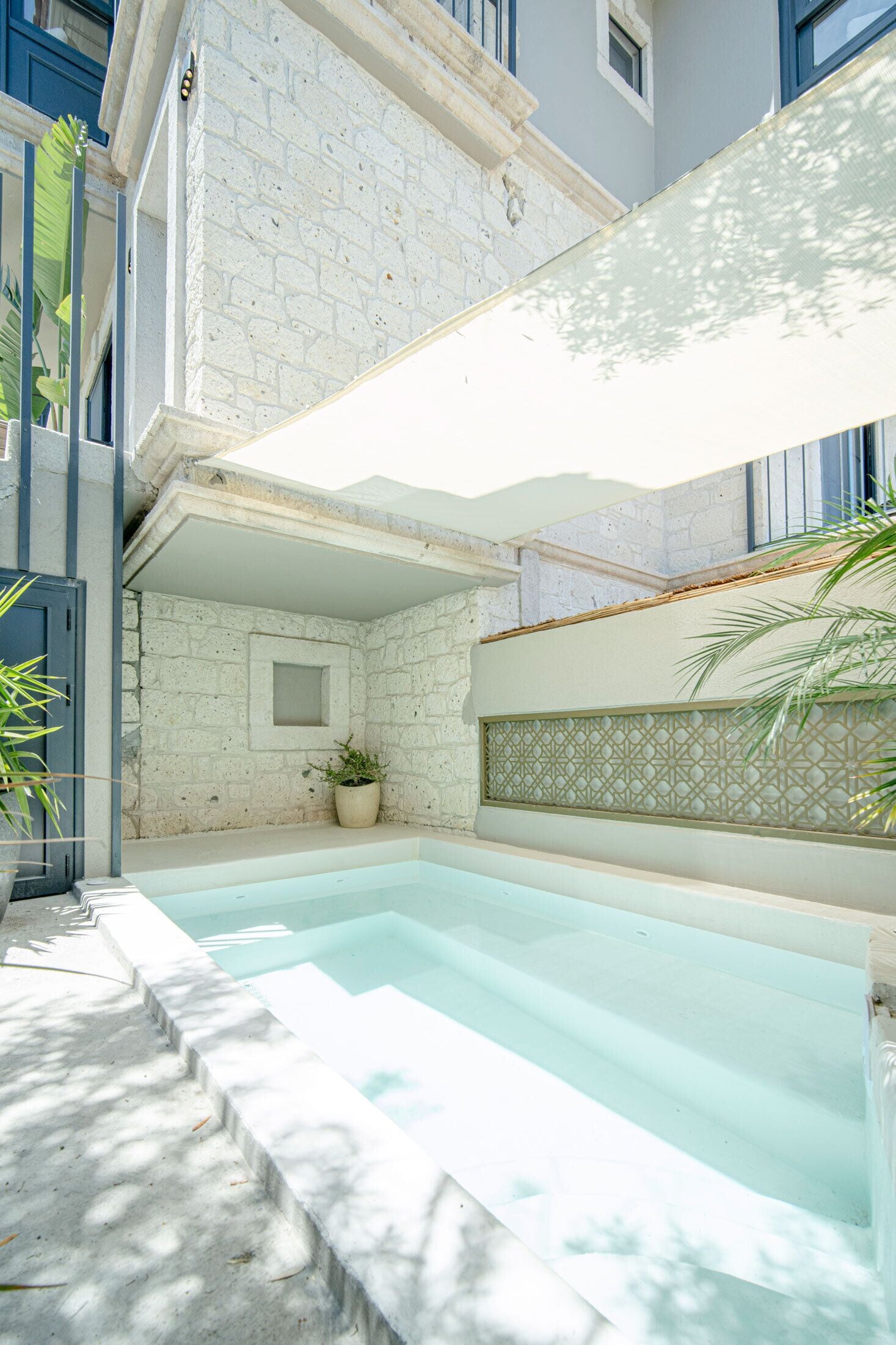 A swimming pool with a stone wall and a potted plant.
