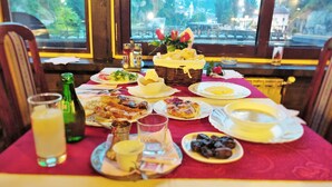 A table set with breakfast items including eggs, toast, and pastries, with a view of a park through a window. - Pansion River (Sarajevo)