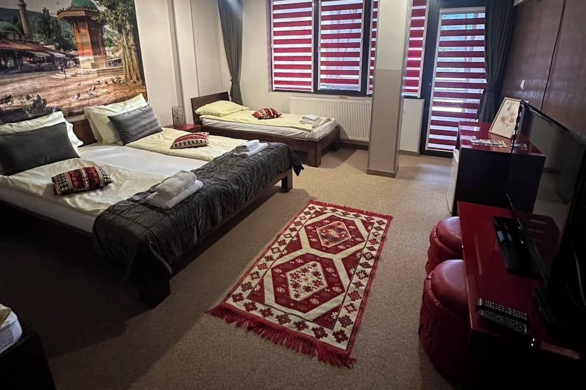 A hotel room with two beds, a red sofa, a TV, and a large window with striped curtains.