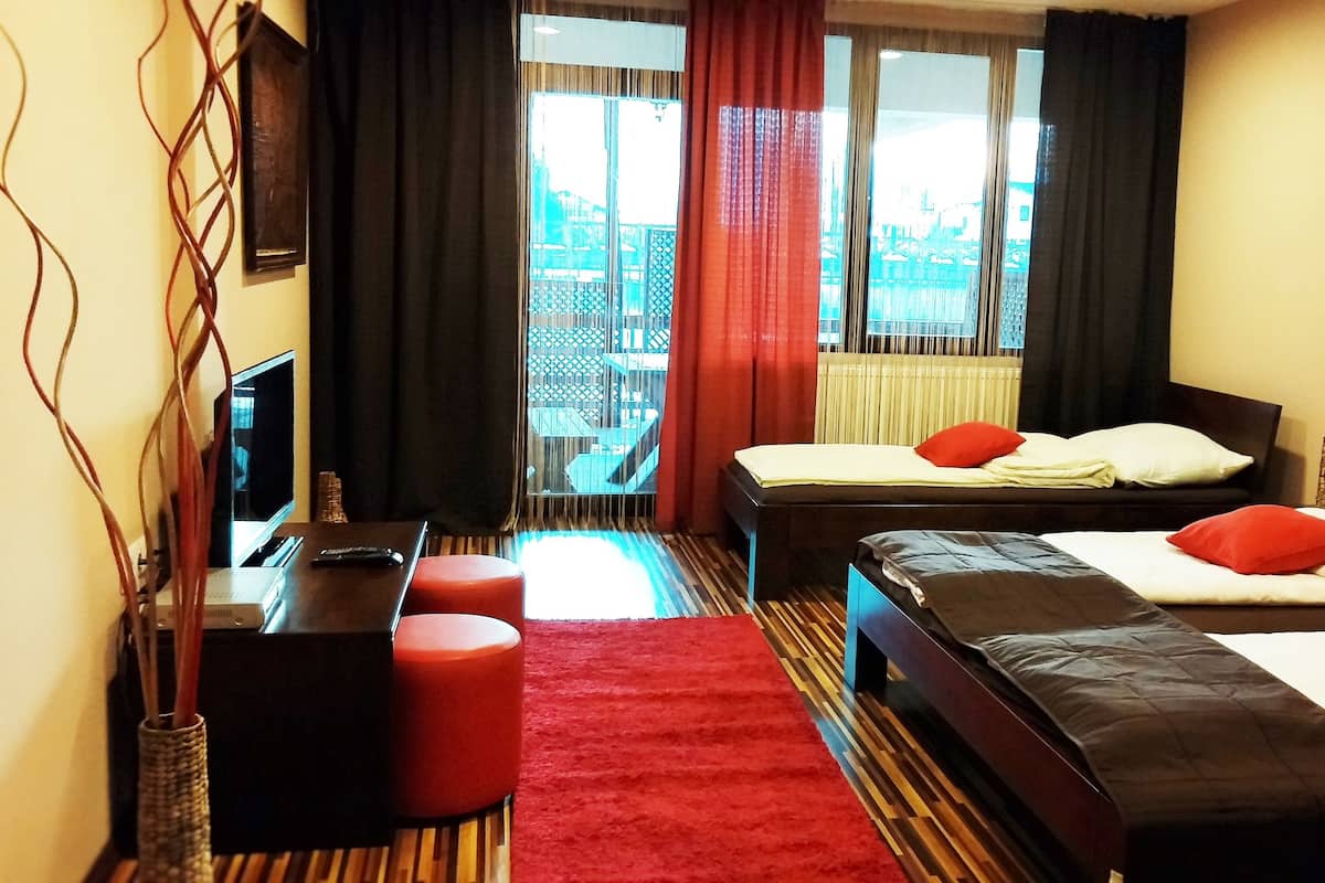 A hotel room with two beds, a desk, a chair, a TV, and a view of the city through large windows.