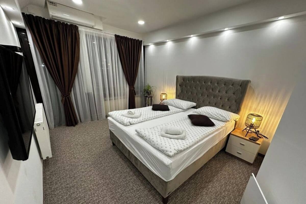 A double bed with a grey headboard, a bedside table with a lamp, and a window with curtains.