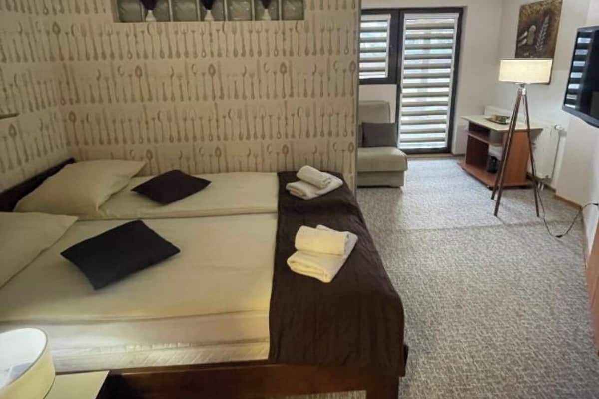 A hotel room with a bed, a bedside table, a lamp, and a window with blinds.