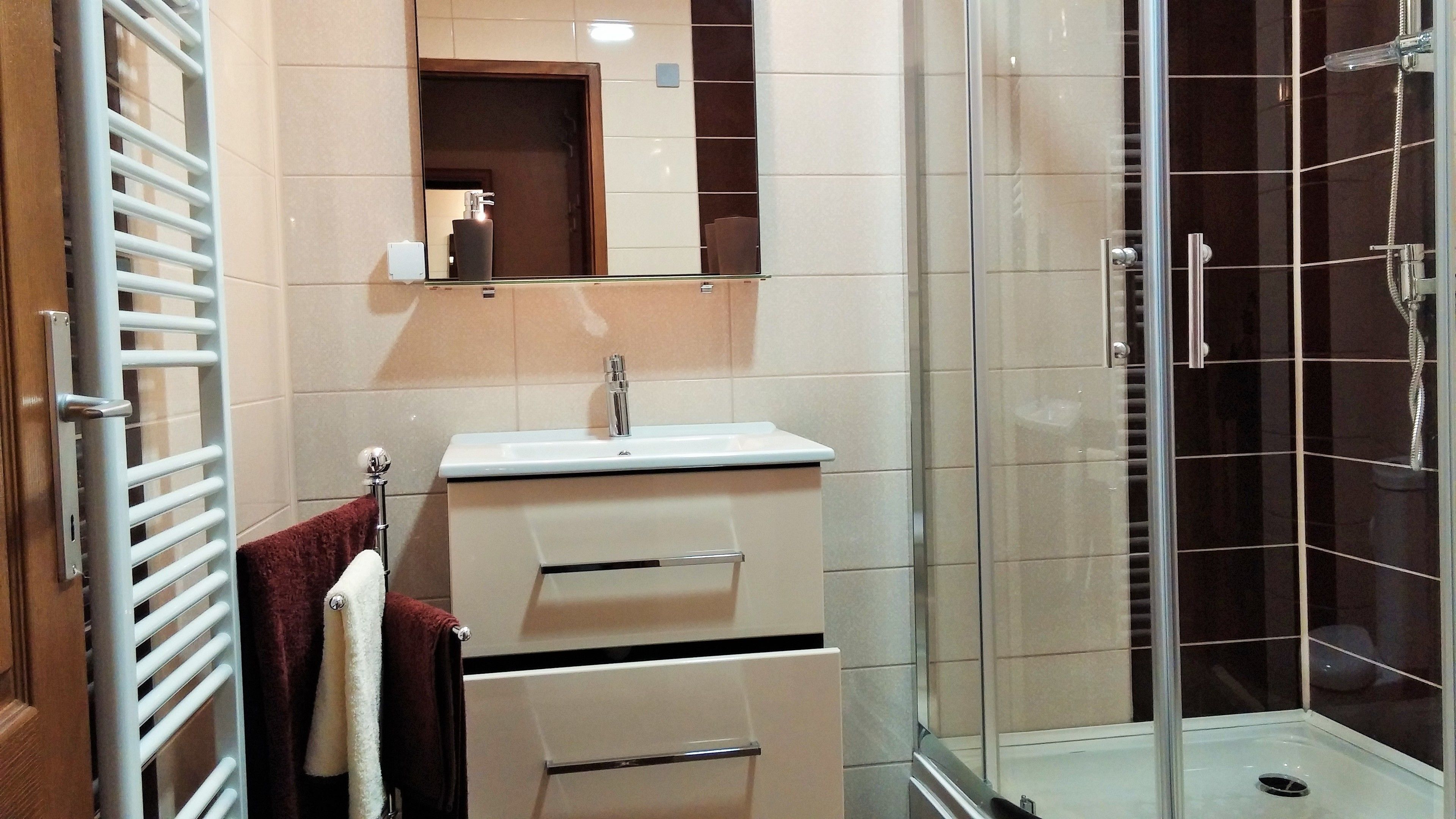 Un baño con cabina de ducha de vidrio, un lavabo blanco y un perchero para toallas.