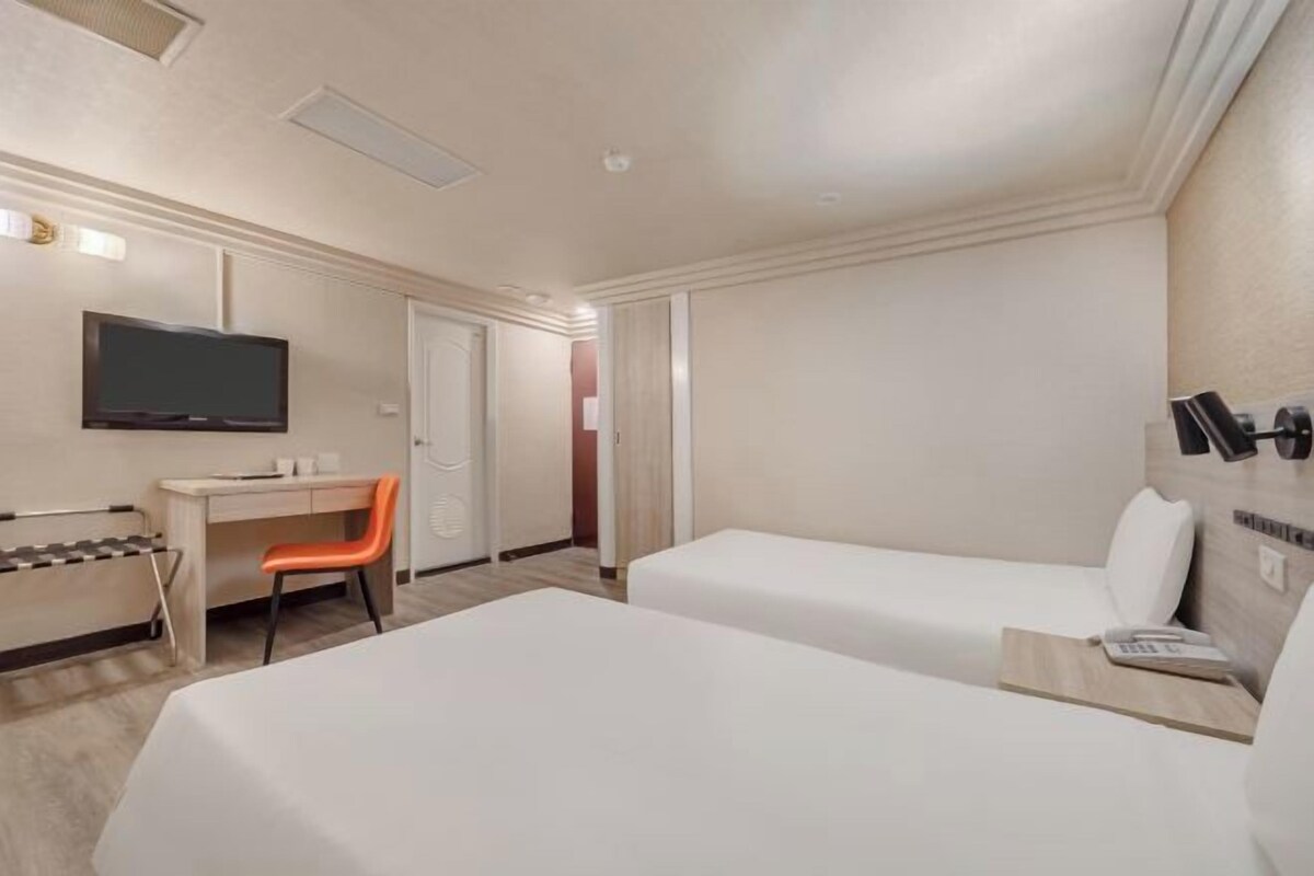 A hotel room with two beds, a desk, a chair, a television, and a door.