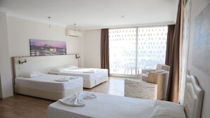 A hotel room with two beds, a sofa, a chair, a large window with curtains, and a cityscape painting on the wall. - Firat Mert Hotel (Cesme)