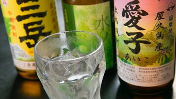 Um copo de água com cubos de gelo, duas garrafas com etiquetas japonesas e uma superfície de madeira.