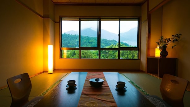 A traditional Japanese room with tatami mats, a low table with a bowl, and a view of mountains through large windows. - Tashiro Bekkan (Yakushima)