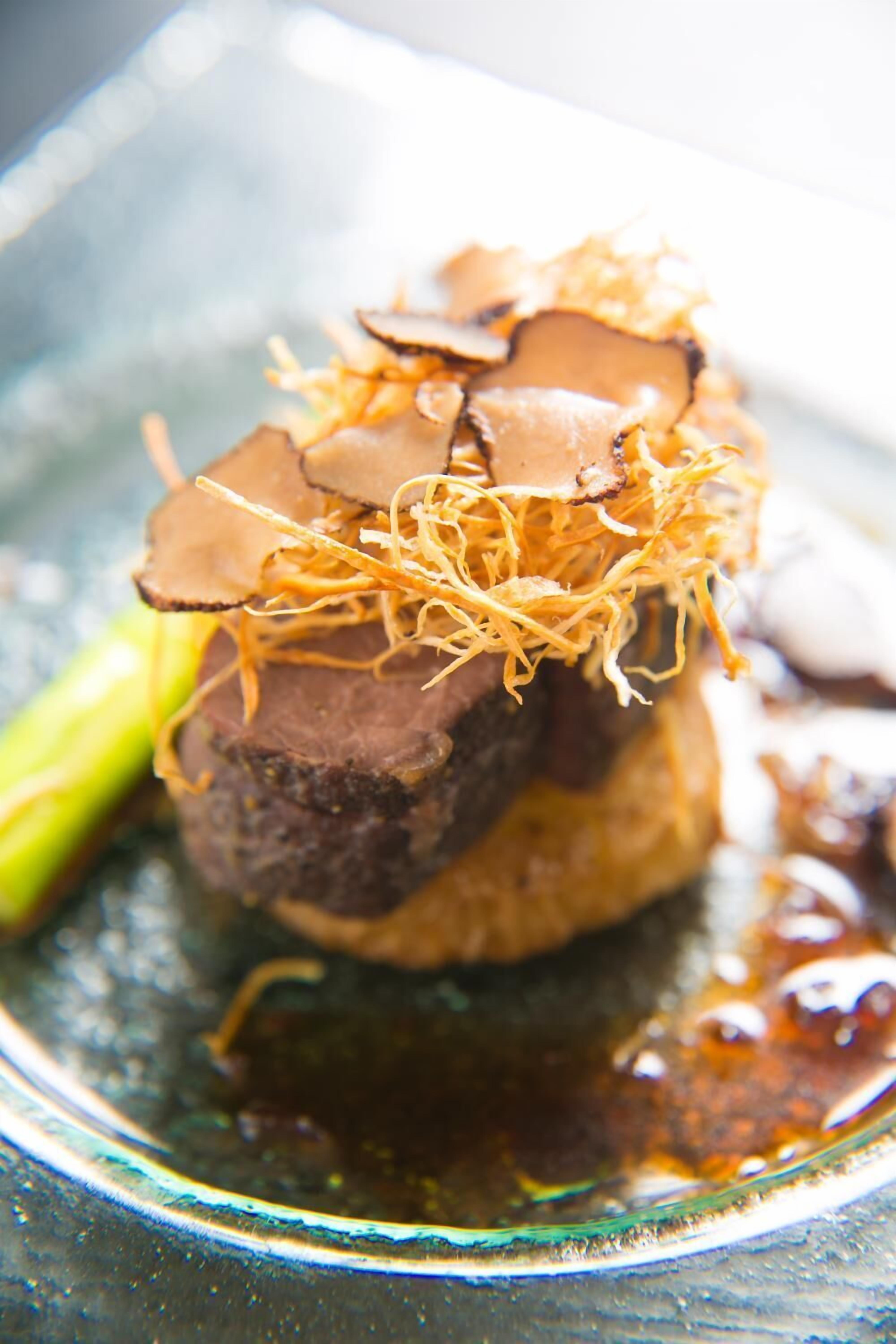 A dish with a piece of meat topped with mushroom slices and thinly sliced vegetables, served on a glass plate.