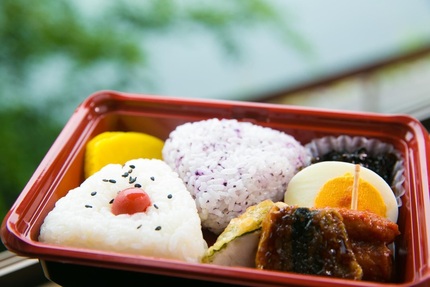 A bento box with rice, egg, meat, and a yellow item.