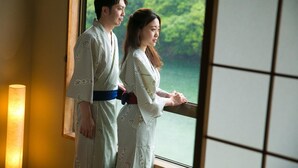 Two people in traditional attire standing by a window with a view of greenery. - Tashiro Bekkan (Yakushima)