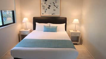 A neatly made bed with a blue throw blanket, two bedside lamps, and a framed abstract artwork above the bed.