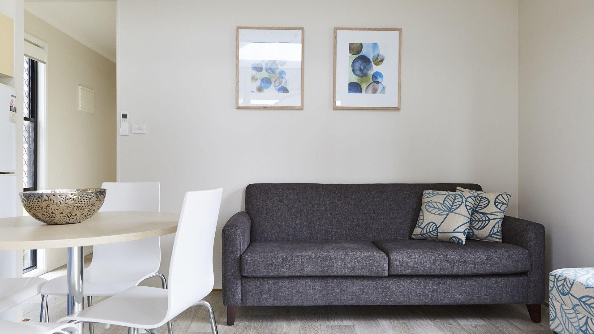 A modern living room with a grey sofa, white chairs, a wooden dining table, and two abstract paintings on the wall.