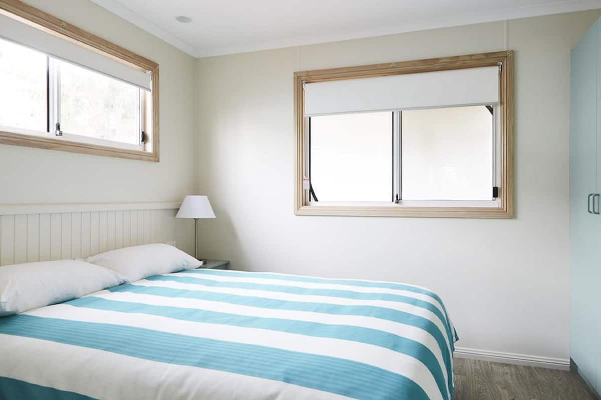 Une chambre à coucher avec un lit, deux fenêtres, une table de chevet avec une lampe et une armoire.