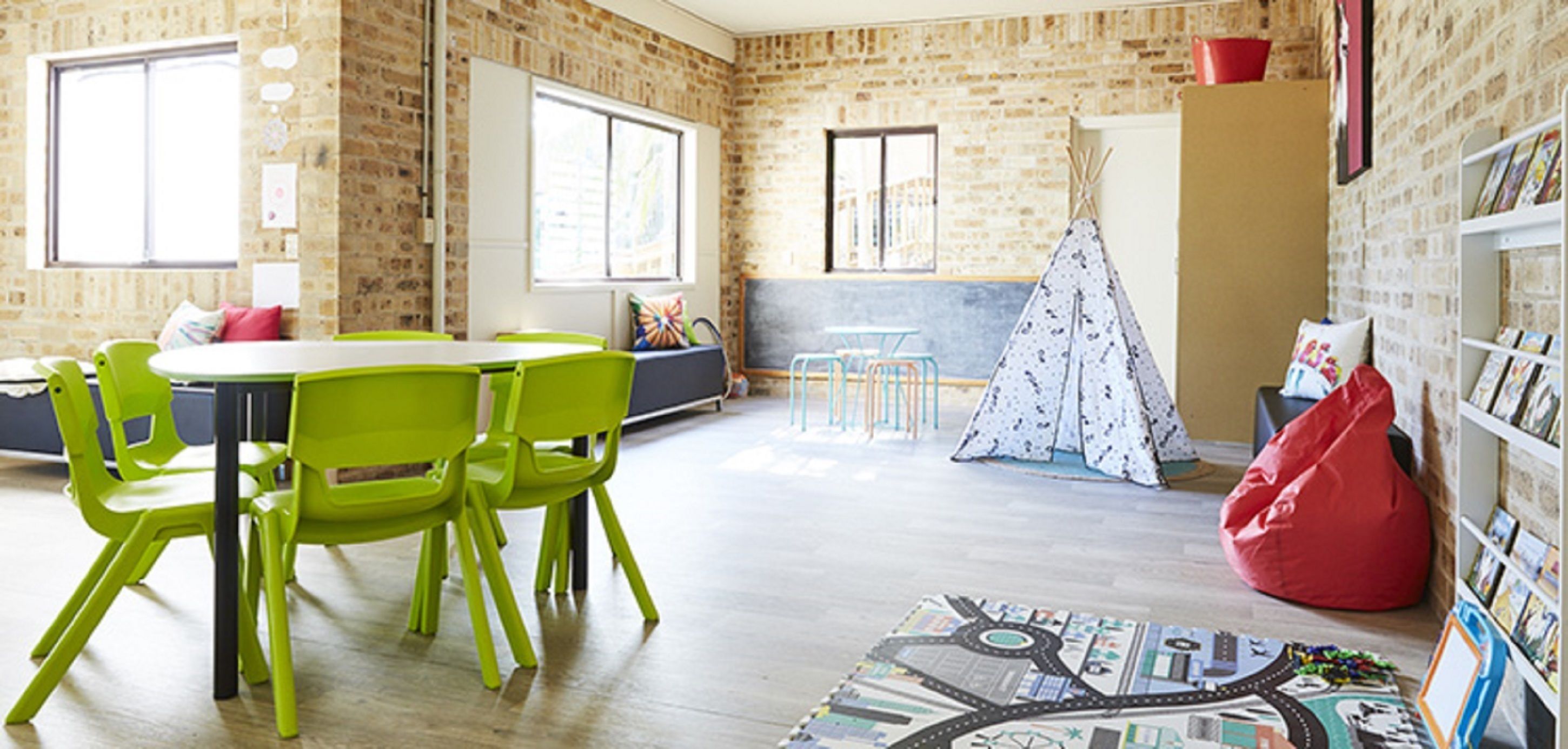 A room with a brick wall, a round table with chairs, a bookshelf, a red bean bag, and a teepee.
