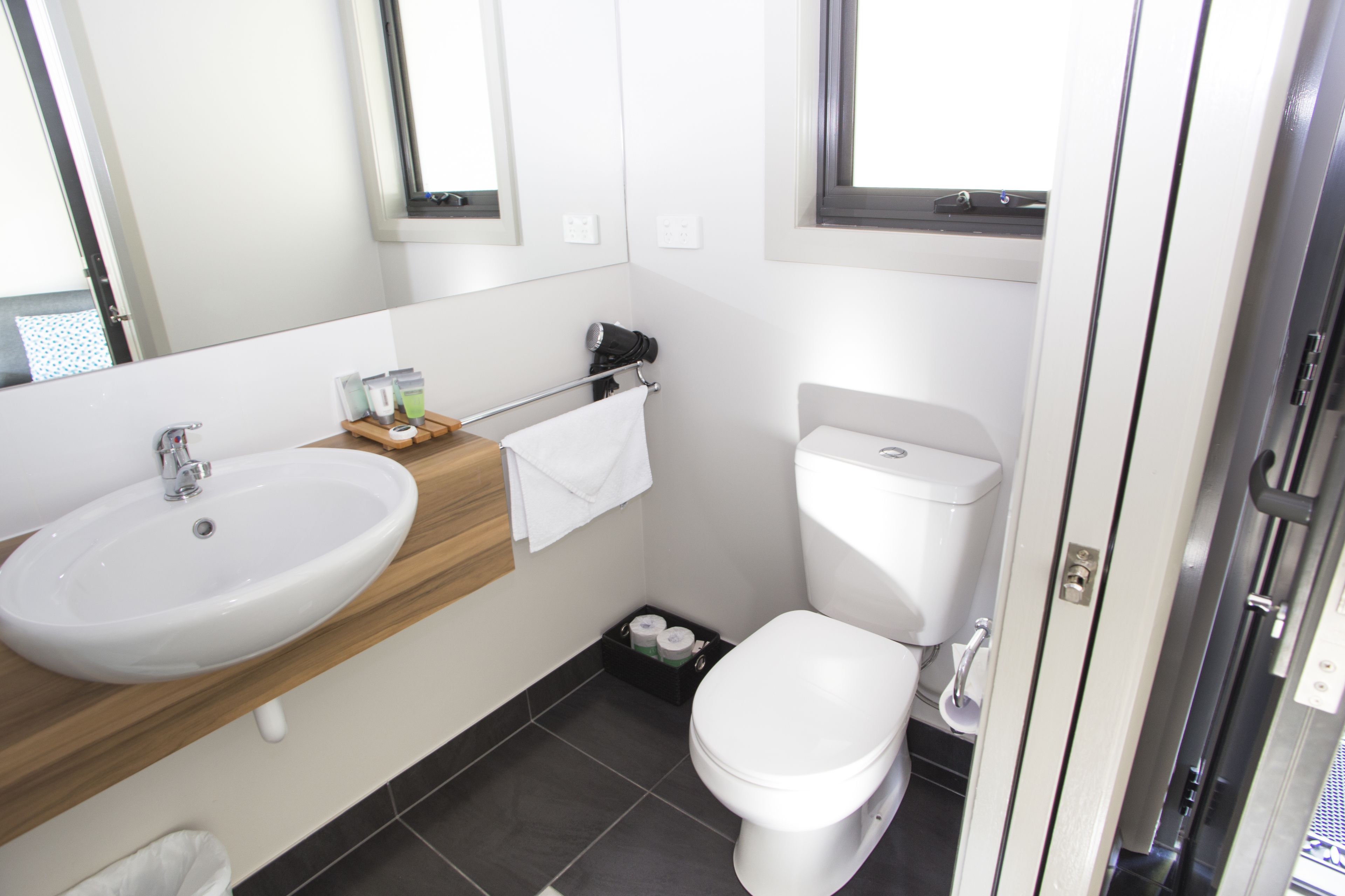 A modern bathroom with a white sink, toilet, and a small window above the toilet.