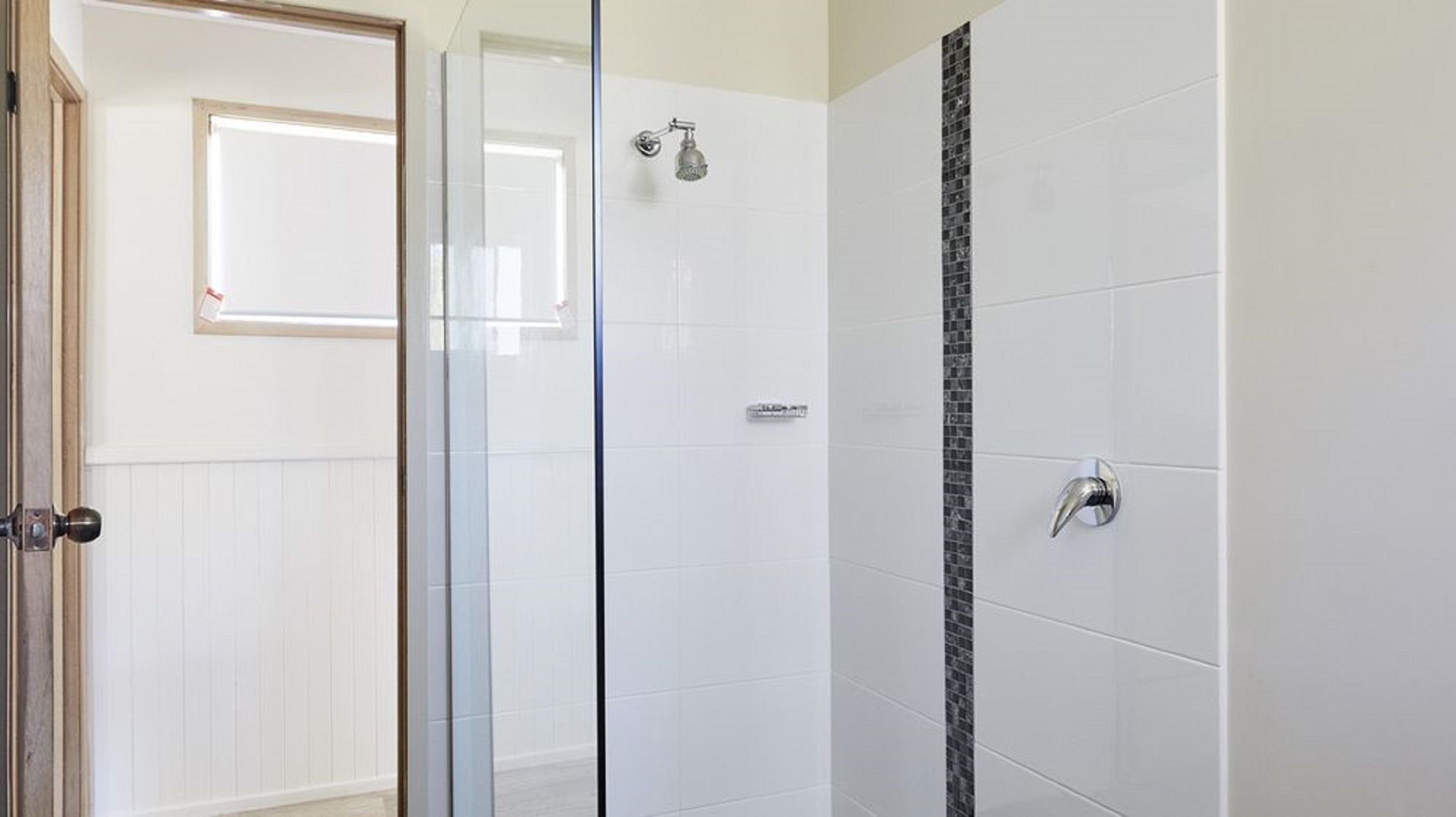 Ein modernes Badezimmer mit Duschkabine aus Glas, weiß gefliesten Wänden und einem dekorativen Akzent in Schwarz.