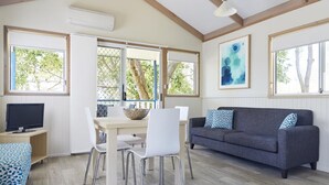 Una habitación con techo de madera, una mesa de comedor con sillas, un sofá gris con cojines estampados y un televisor sobre un mueble de madera.