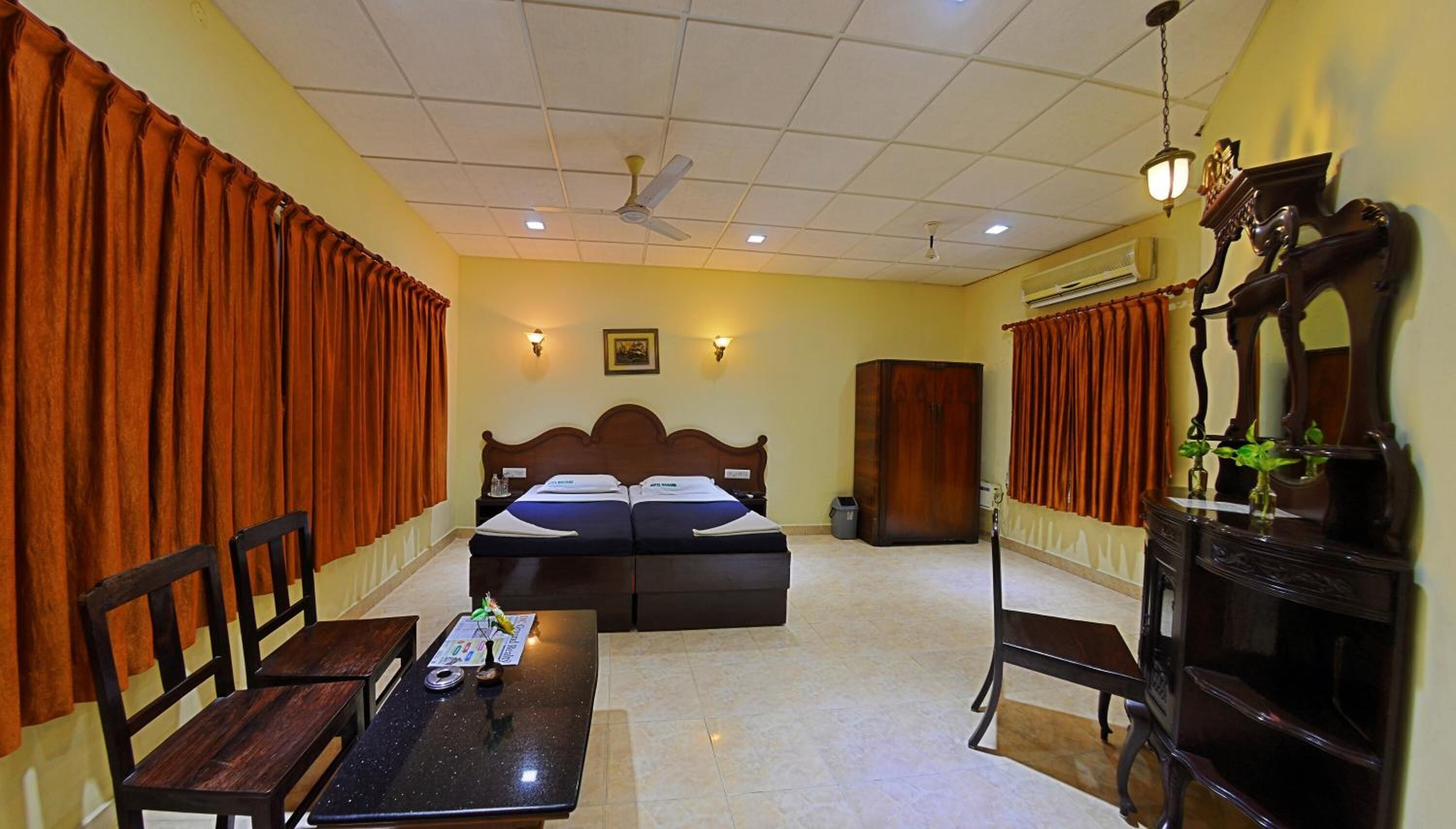 A hotel room with a double bed, two bedside tables, a desk, a chair, a wardrobe, a ceiling fan, and a mirror.