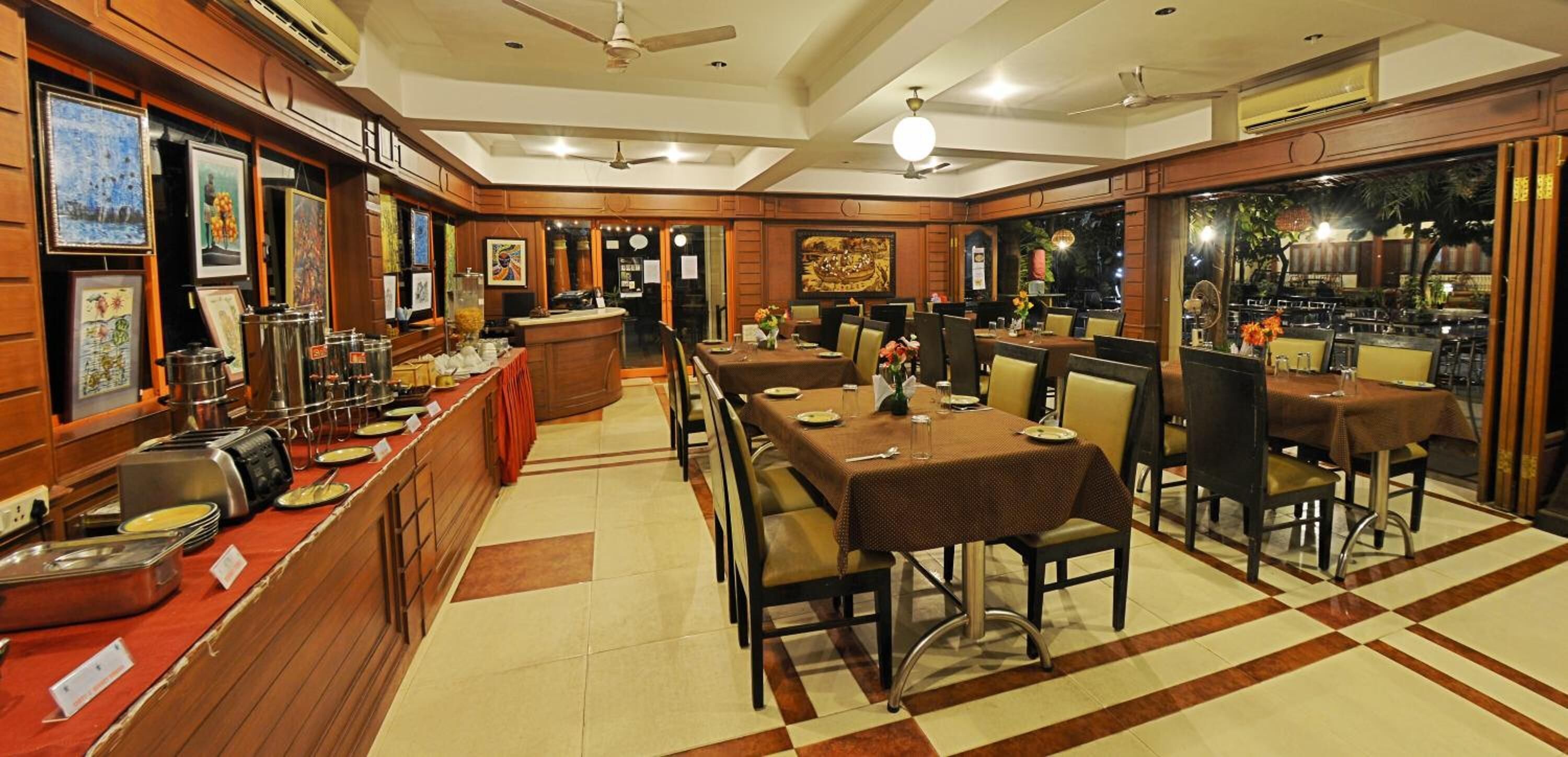 A restaurant with a buffet setup, multiple dining tables, and a counter with food items.