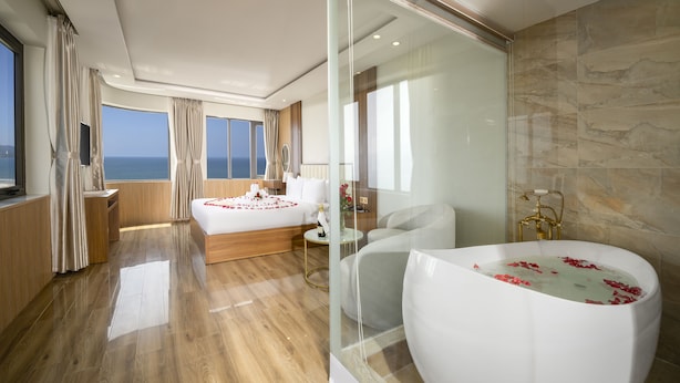 A modern hotel room with a large bed, a sitting area, and a bathtub filled with rose petals. - 7 Seven Sea Hotel  (Da Nang)