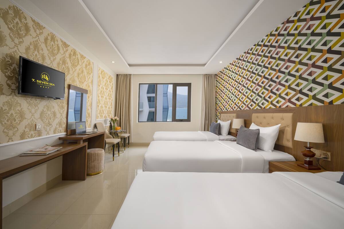 A hotel room with two beds, a desk with a laptop, a TV, and a patterned wall.