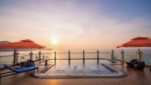 A rooftop pool with sun loungers and umbrellas, overlooking a body of water at sunset. - 7 Seven Sea Hotel  (Da Nang)