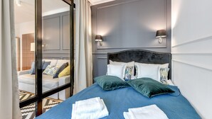 A neatly made bed with blue bedding and white towels, a dark headboard, and two wall-mounted lamps. - GRANO APARTMENTS Gdańsk Motława SPA & Wellness (Gdansk)