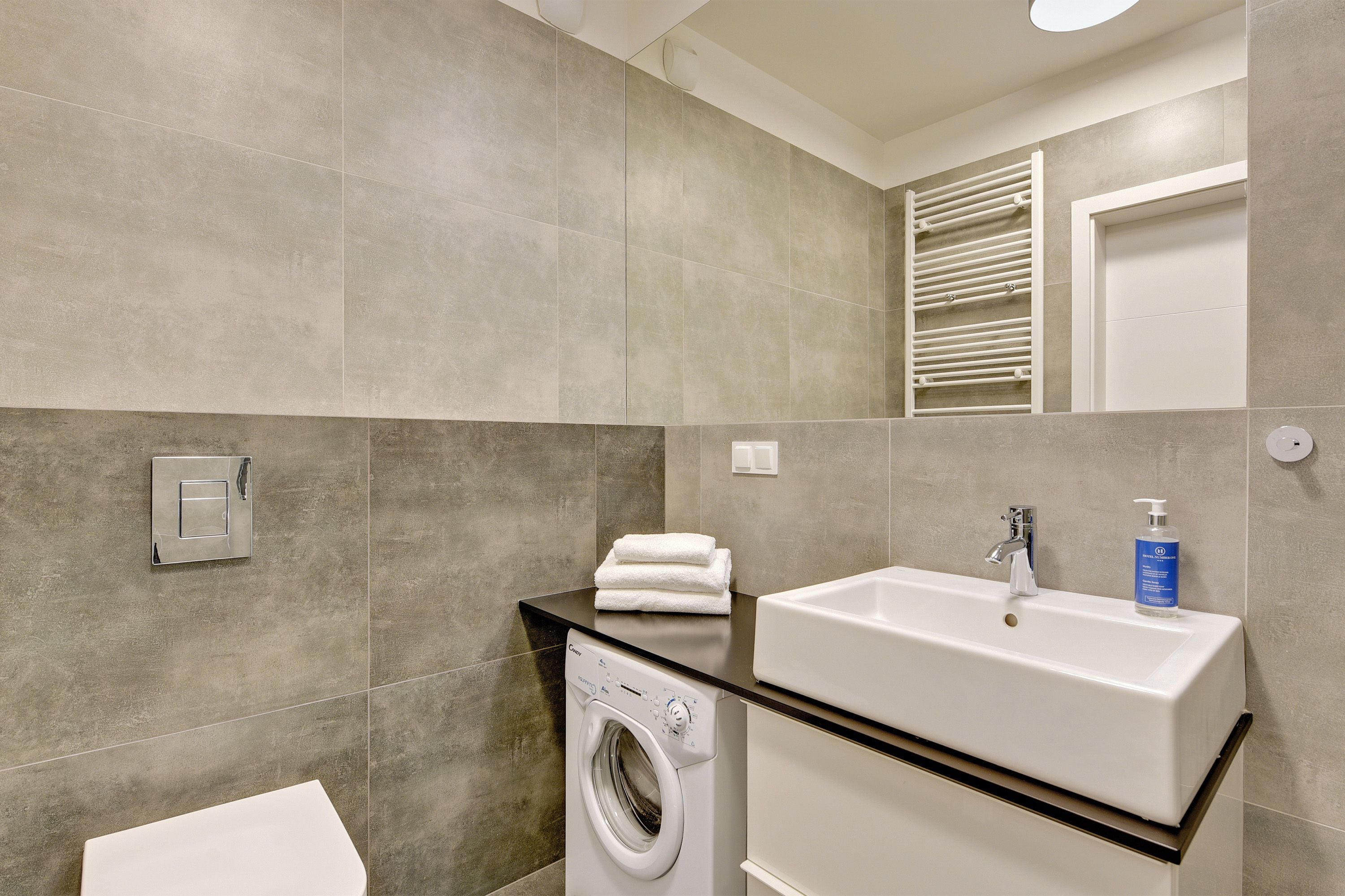 Une salle de bain moderne équipée d’un lave-linge, d’un lavabo et d’un porte-serviettes.
