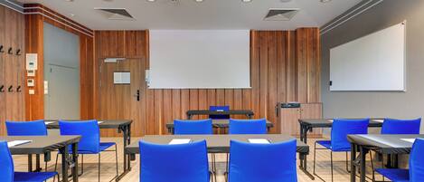 A conference room with wooden panel walls, a large projection screen, and blue chairs around tables.