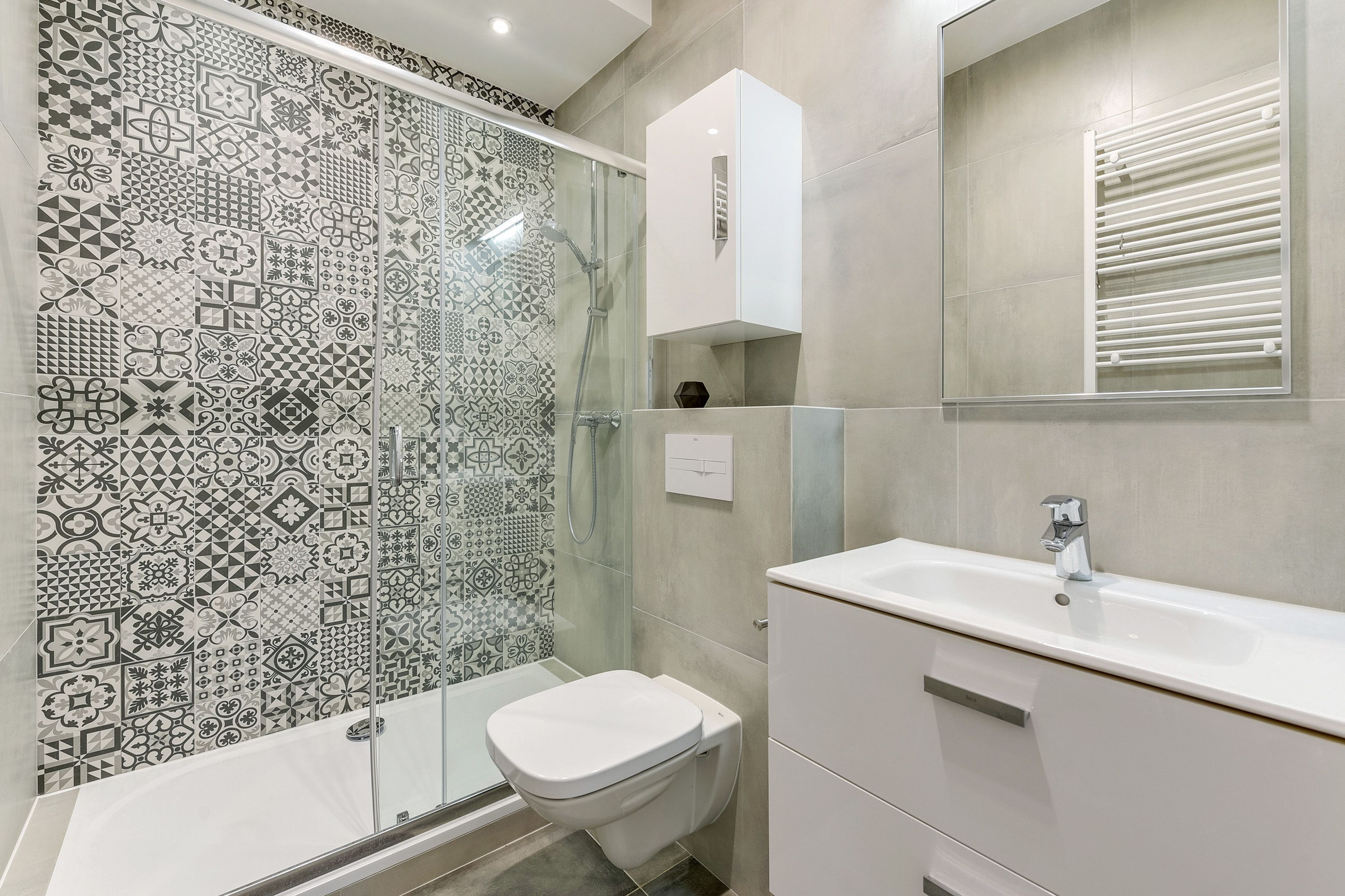 A bathroom with patterned tiles, a glass shower enclosure, a white toilet, and a sink with a cabinet.
