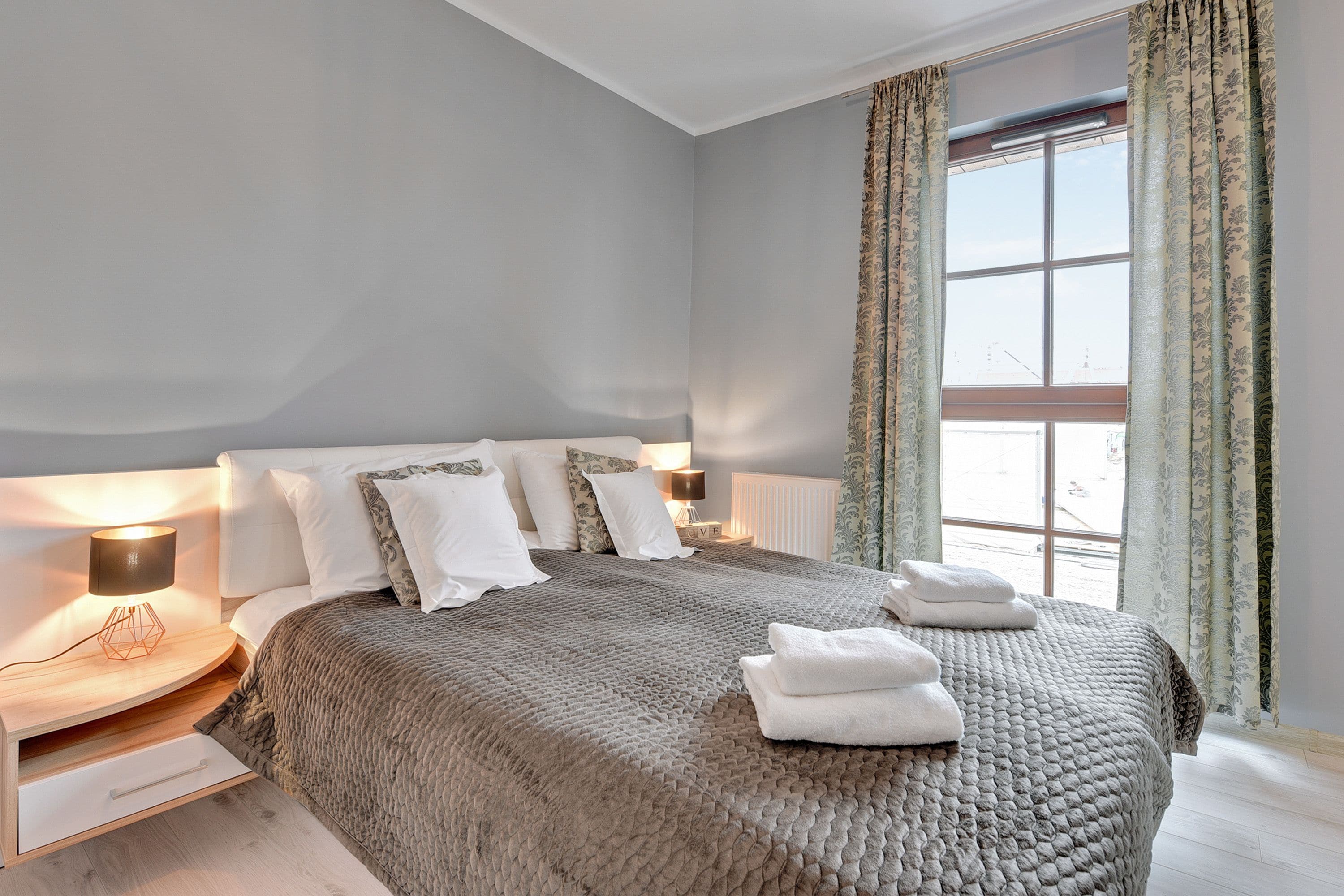 A bedroom with a large bed, bedside lamps, a window with curtains, and a view outside.