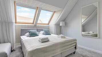 Un dormitorio con una cama grande, dos ventanas, un espejo y una lámpara de noche.