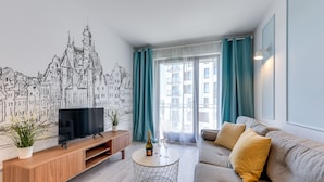A modern living room with a flat-screen TV, a wooden console table, a round coffee table, and a grey sofa with yellow cushions. - GRANO APARTMENTS Gdańsk Motława SPA & Wellness (Gdansk)