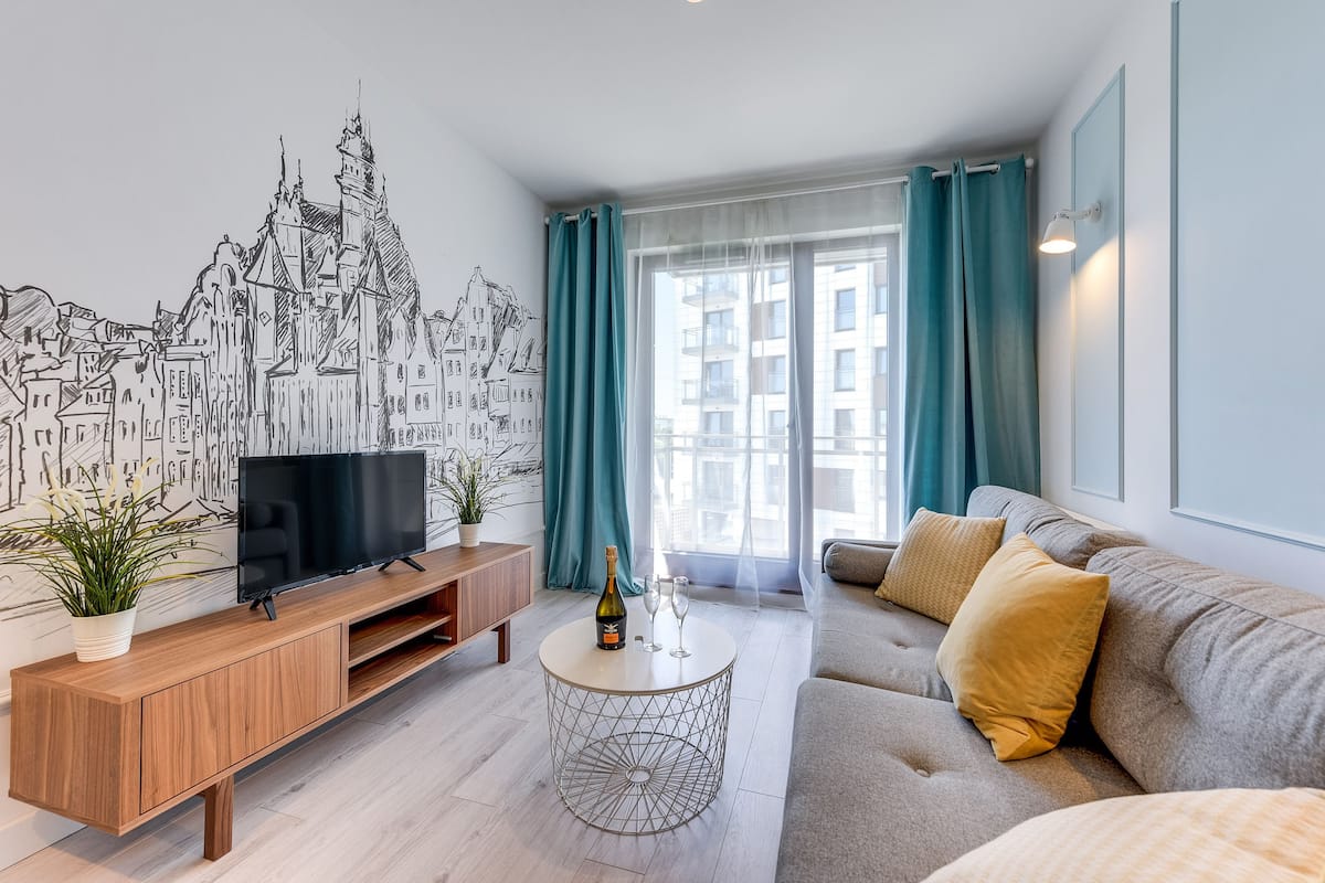 Un salon moderne avec un téléviseur à écran plat, une console en bois, une table basse ronde et un canapé gris agrémenté de coussins jaunes.