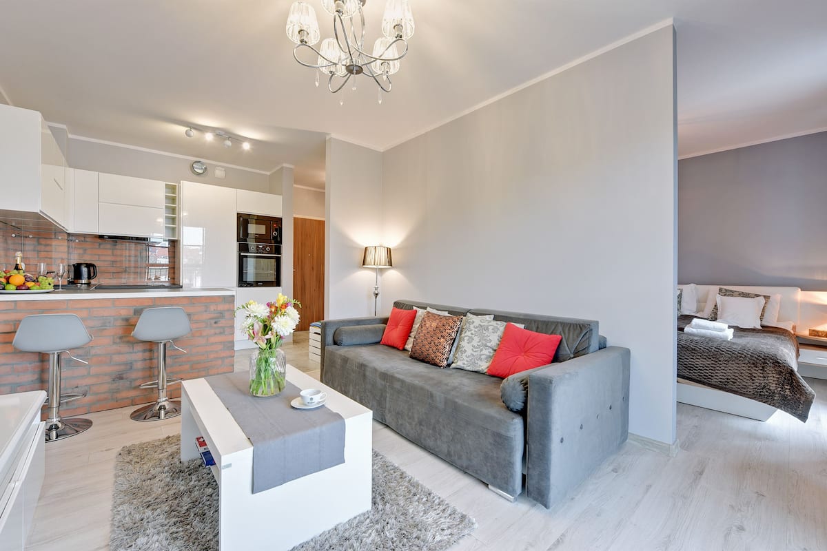 Un salon moderne avec un canapé gris, une table basse et un coin repas équipé de tabourets de bar.