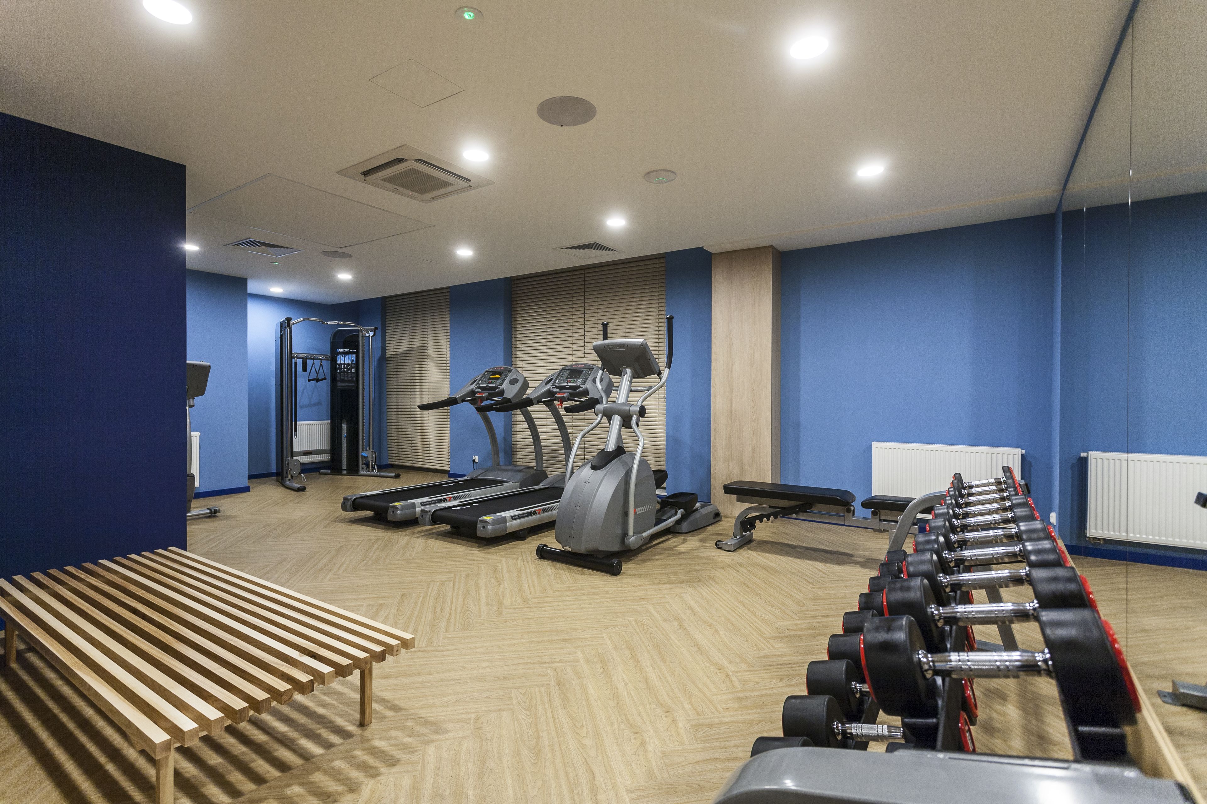 Et fitnessrum med løbebånd, crosstrainere og en bænk.