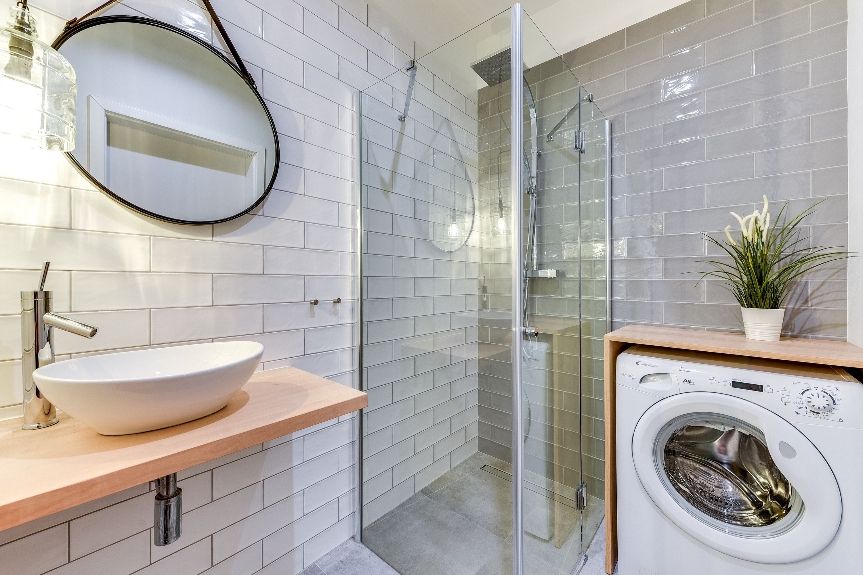 Ein modernes Badezimmer mit einem weißen Waschbecken, einer Duschkabine aus Glas und einer integrierten Waschmaschine.
