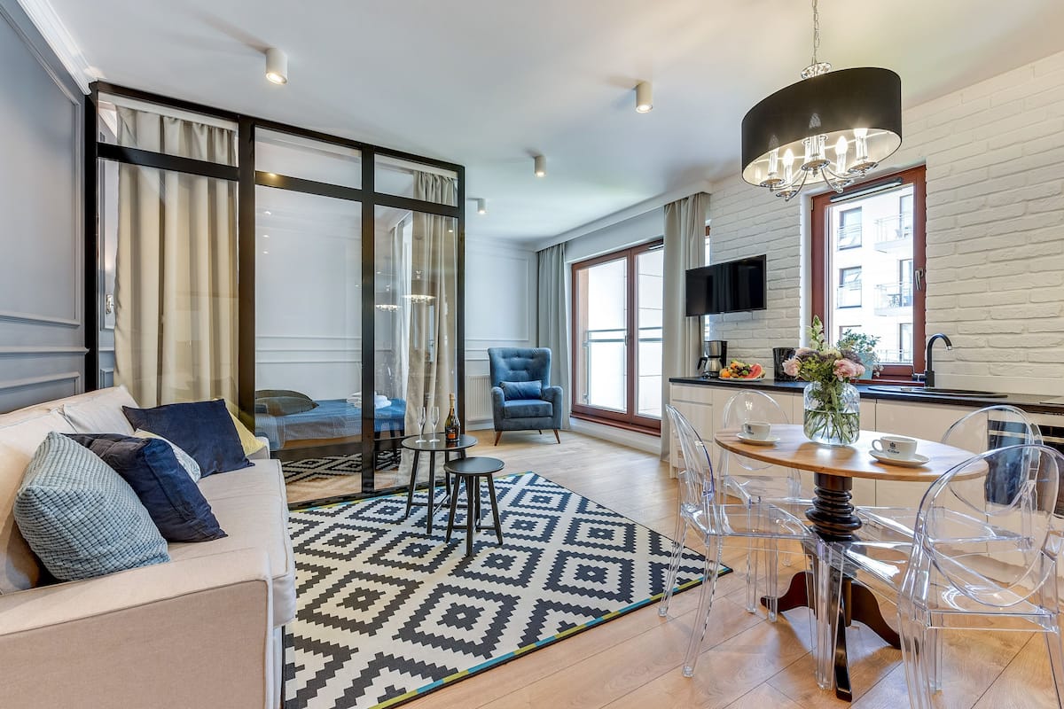 Un salon moderne avec un canapé, un tapis à motifs, une table à manger avec des chaises transparentes et un lustre.