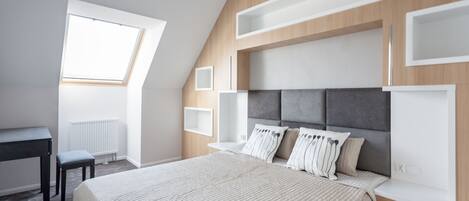Quarto com cama grande, escrivaninha e claraboia.